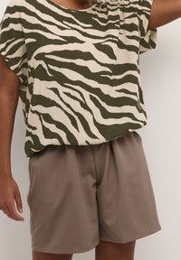 Bluzka z krótkim rękawem w kolorze oliwkowym i kremowym w paski zebry, w zestawie z luźnymi, jasnobrązowymi szortami. Tkanina ma teksturowany wygląd.