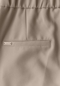Beige tyg med en slät yta, har en liten märkesetikett "Street One" på en ficka med kant. Designen inkluderar en draperad midjedetalj.