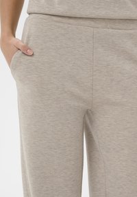 Svetlo béžové jogger nohavice vyrobené z mäkkej, štruktúrovanej tkaniny, s bočnými vreckami a voľným strihom pre pohodlie.