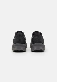 Baskets de sport noires avec un dessus en tricot texturé, un col rembourré et une semelle en caoutchouc striée pour une bonne adhérence. Présente un design minimaliste.