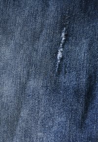 Tela de mezclilla azul oscuro con una ligera área desgastada y hilos blancos visibles, mostrando un patrón de tejido texturizado.