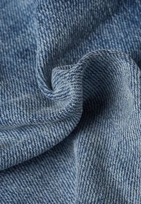 Svijetloplava traper tkanina s teksturiranom prepletom, koja prikazuje mekanu, glatku površinu i blagi sjaj s dijagonalnim žljebovima.