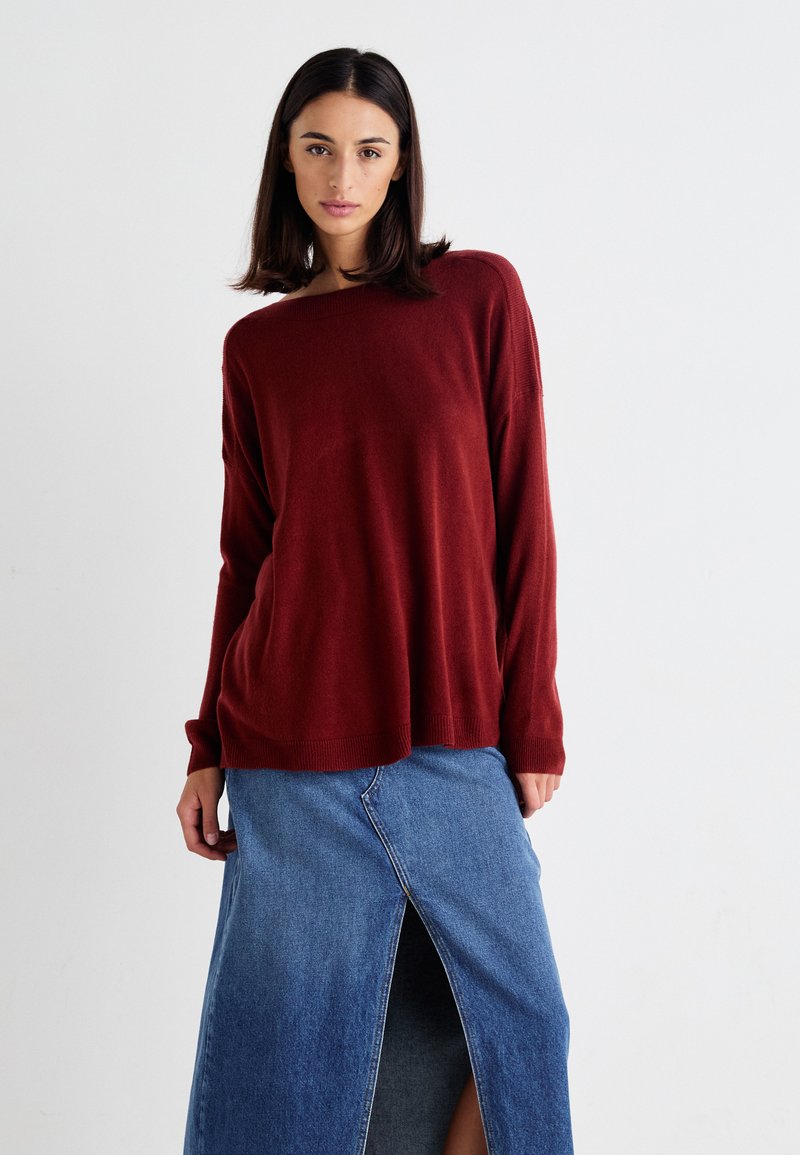Bordeaux gebreide trui met een wijde halslijn en lange mouwen, gecombineerd met een denim rok met een split aan de voorkant in een lichte blauwtint.