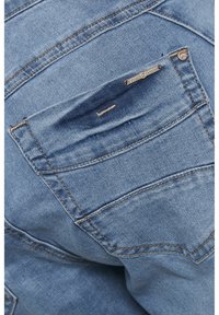 Ljusblå denimjeans med en bakficka som har en liten metalltagg som står "Cream Denim." Synlig sömnad och texturdetaljer.