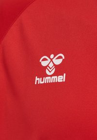 Czerwona tkanina z białym stylizowanym logo pszczoły i napisem „hummel” nadrukowanym poniżej na ubraniu sportowym.