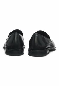 Mocassins en cuir noir avec une texture lisse, un talon bas, un bout rond et un design minimaliste. La vue arrière met en avant un détail de couture subtil.