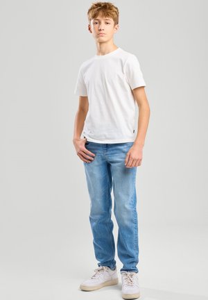 T-shirt en coton blanc associé à un jean bleu clair. Le jean a une coupe droite, et la tenue est complétée par des baskets blanches.