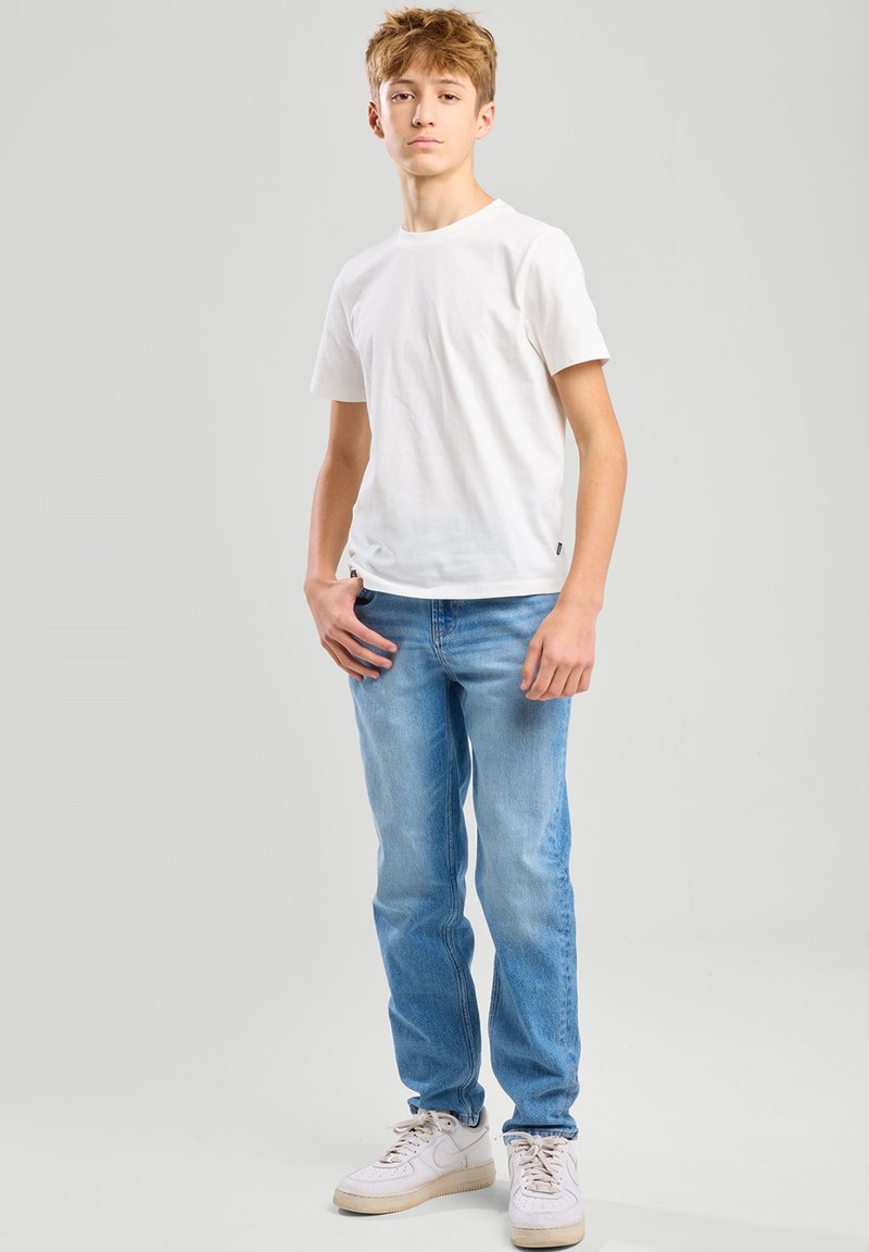 T-shirt en coton blanc associé à un jean bleu clair. Le jean a une coupe droite, et la tenue est complétée par des baskets blanches.
