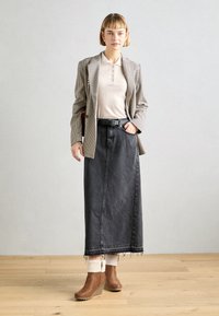 Saia maxi de denim cinza com bainha desfiada, combinada com um blazer xadrez e uma polo creme. Botas de cunha castanhas com detalhes em pele sintética completam o look.