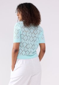 Maglione azzurro chiaro a maglia con motivo a diamante, maniche corte e orlo a coste. Il retro presenta un design a trama aperta.