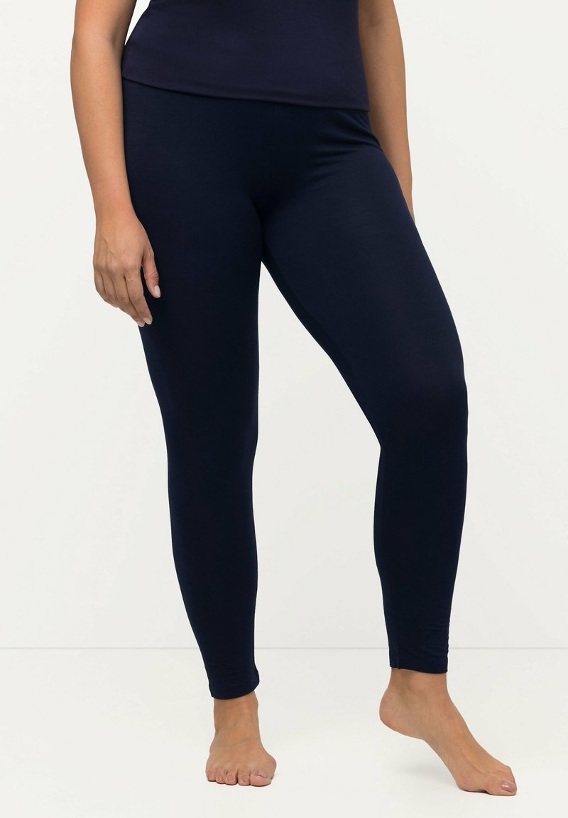 Leggings blu navy in un materiale liscio e elastico, caratterizzati da un design aderente e un taglio lungo, indossati da un modello con piede nudo.