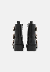 Czarne skórzane botki za kostkę z złotymi akcentami, charakteryzujące się grubą podeszwą i bocznymi zamkami błyskawicznymi dla łatwego zakładania. Gładka tekstura i wyraźna forma.
