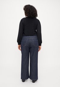 Wide-leg dark blue denim jeans paired with a textured black top featuring puffed sleeves. Visible stitching and pockets are noted.