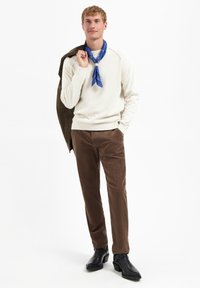 Witte geribde trui, bruine corduroy broek, blauwe bandana, donkere jas over de schouder, zwarte laarzen. Eenvoudig ontwerp, warme texturen.