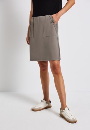 Grå knälång kjol i mjukt tyg, med två framfickor och knappdetaljer. Matchas med vita sneakers för en avslappnad look.