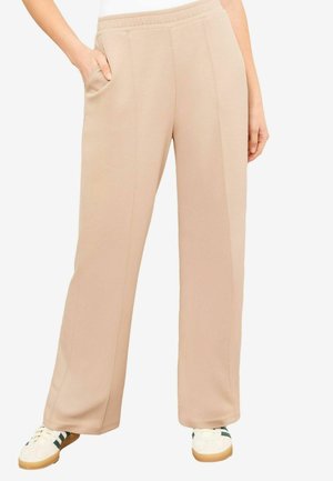 Pantalons de survêtement larges beiges avec une finition texturée, dotés d'une taille élastique et de poches latérales. Associés à des baskets blanches.
