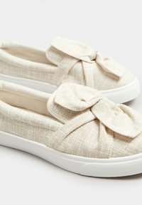Scarpe slip-on beige testurizzate con un accento a fiocco, dotate di una tomaia in tessuto leggero e di una suola in gomma bianca.