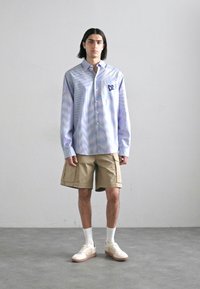 Light blue striped long-sleeve shirt with button-up front and chest pocket, paired with beige cargo shorts and light-colored sneakers.