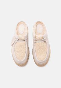 Lys beige slip-on sko med en fluffy kremfarget innside, gummisåle og teksturert overflate. Har minimal snøring og merkede detaljer.