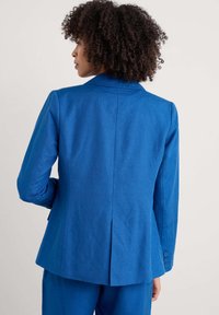 Niebieski żakiet z teksturowanej tkaniny, z pojedynczym rozcięciem z tyłu, klapami i guzikami na rękawach.