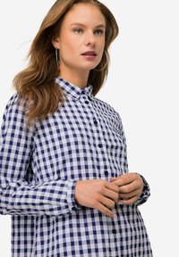Camicia a quadri blu e bianchi con colletto button-down. Presenta maniche lunghe e bottoni blu. Tessuto morbido, design casual.