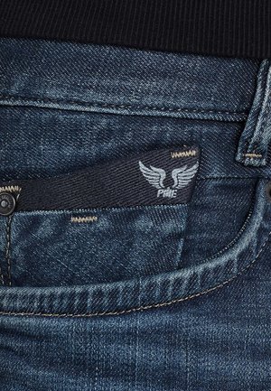 Denim jeans with a dark blue wash, featuring a visible black label with wing graphic and stitching details on waistband and pocket.