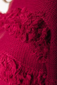 Un tissu tricoté rouge présente un motif texturé avec des accents effilochés le long des bords, offrant une apparence douce et chaleureuse.