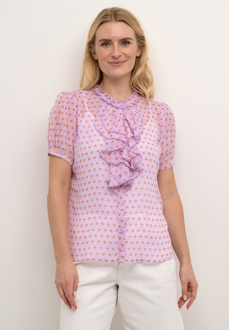 Helllila Bluse mit Diamantmustern in Orange und Pink, mit gerafftem Vorderteil, kurzen Puffärmeln und Knopfschluss.