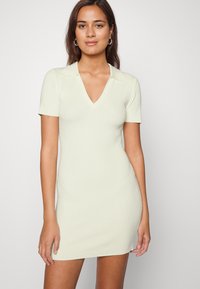 Vestido de tricô de mangas curtas em verde-claro com decote em V e gola. Silhueta ajustada com textura canelada e brilho subtil. Design minimalista.