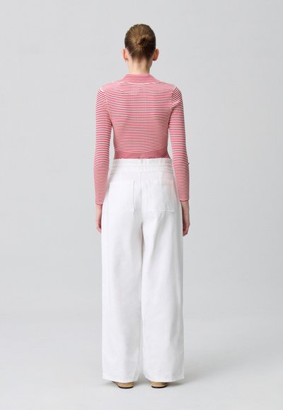 Un top de rayas rojas y blancas de manga larga combinado con pantalones amplios blancos, con bolsillos traseros y un acabado texturizado. Zapatos de plataforma de madera.