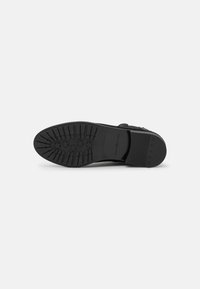 Suela de zapato de goma negra con un patrón de agarre texturizado que presenta estrellas en relieve y bordes suaves. Material duradero, diseñado para tracción y estabilidad.
