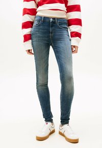 Skinny jeans in een middelblauwe wassing, gemaakt van denim met subtiele vervaging. Draagt een rood-wit gestreept trui en witte sneakers.