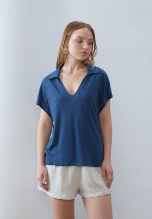 Top azzurro a maniche corte con scollatura a V e colletto, realizzato in un tessuto leggero. Abbinato a pantaloni corti bianchi con texture, dotati di una vita elastica.