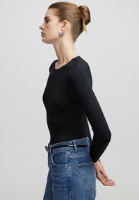 Zwarte lange mouwen bodysuit gecombineerd met hoog-waisted blauwe spijkerbroeken; heeft een ronde halslijn en een aangesloten ontwerp. Zilveren accessoires zichtbaar.