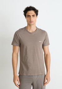 T-shirt à col rond à manches courtes en coton taupe avec un branding minimal. Texture lisse et coupe décontractée, associé à un pantalon assorti.