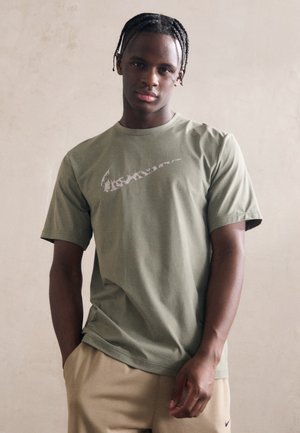 Tricou scurt cu mânecă, de culoare verde măsliniu, din bumbac, având un logo Nike alb pe piept. Design simplu, lejer, cu un decolteu rotund.