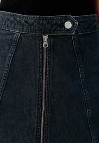 Gonna in denim scuro con zip frontale, vita ampia e cuciture dettagliate. Il tessuto ha una finitura leggermente strutturata.