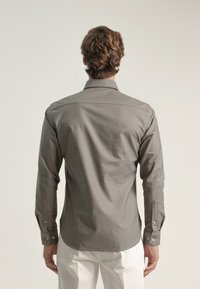 Camisa de manga larga gris con cuello clásico, puños abotonados y un diseño de espalda recta. Tela suave con un acabado mate.