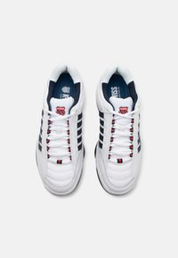 Baskets de sport blanches avec une construction rembourrée, des rayures marine, des accents rouges et bleus, et un logo sur la languette.