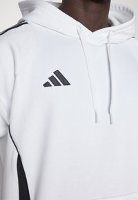 Weißer Hoodie mit schwarzen seitlichen Akzenten und einem schwarzen, gestickten Adidas-Logo auf der Brust. Verfügt über eine Kapuze mit Kordelzug und angenehm weichem Stoff.