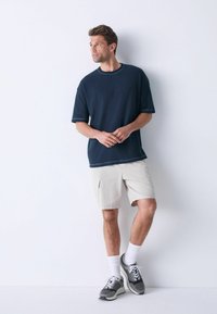 Marineblå struktureret kortærmet skjorte med kontrasterende kant, parret med beige cargo shorts. Båret med grå sneakers og hvide sokker.