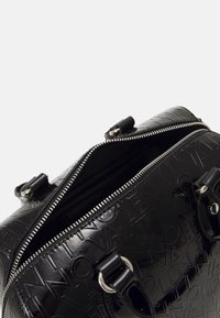 Black patent leather handbag with embossed logo texture, dual handles, and a silver zipper closure. Inside appears spacious and lined.