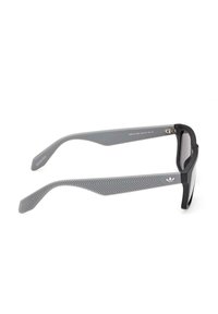 Occhiali da sole grigi con una robusta montatura nera. Le tempie presentano un motivo a trama grigia e un piccolo logo bianco. Le lenti sono scure e riflettenti.