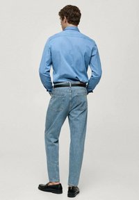 Lichtblauwe spijkerbloes gecombineerd met lichtblauwe spijkerbroek. De outfit heeft een donkere riem en zwarte schoenen, met een gladde textuur en een casual pasvorm.