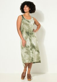 Grünes Tie-Dye-Midi-Kleid mit Rundhalsausschnitt und ärmellosem Design. Glatte Stoffe mit lockerer Passform, kombiniert mit braunen Clogs.