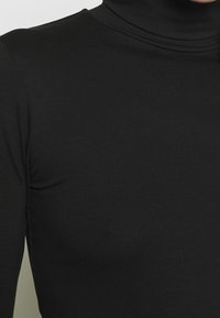 Svart polotröja i ett mjukt, stretchigt tyg. Har hög halsringning och en figurnära design, lämplig för lager-på-lager.