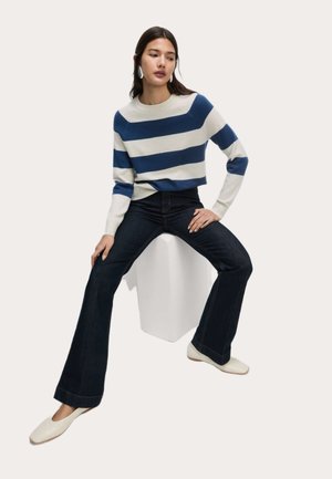 Pull rayé bleu marine et crème, associé à un jean évasé foncé et des ballerines crème. Texture tricot lisse et finition en denim solide.