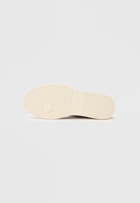 Cream-colored rubber shoe sole with textured grip and circular pattern near toe, embossed with the brand name "BOSS" in the center.