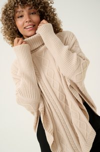 Übergrößenpullover in hellbeige, mit einem gerippten Rollkragen und einem strukturierten Rautenmuster, weiten Ärmeln und seitlichen Schlitzen.