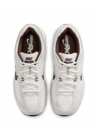 Ténis Nike Moto 2K brancos com um upper em malha texturizada, pormenores em castanho e atacadores, apresentando o logo da Nike na língua e no lado.